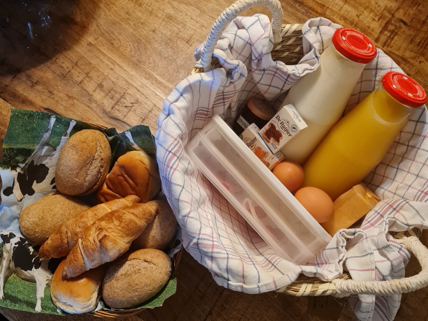 Der Frühstückskorb: frische Brötchen, Croissants, Eier, Milch, Saft und Aufschnitt in einem Korb mit Geschirrtuch